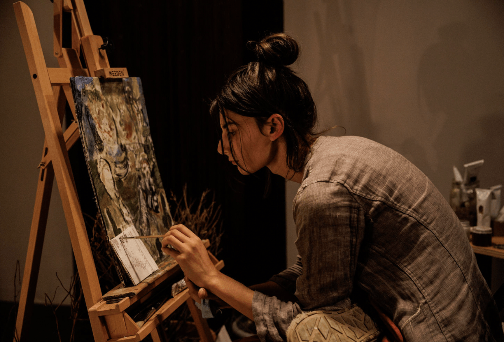 A person hunched over paints at an easel