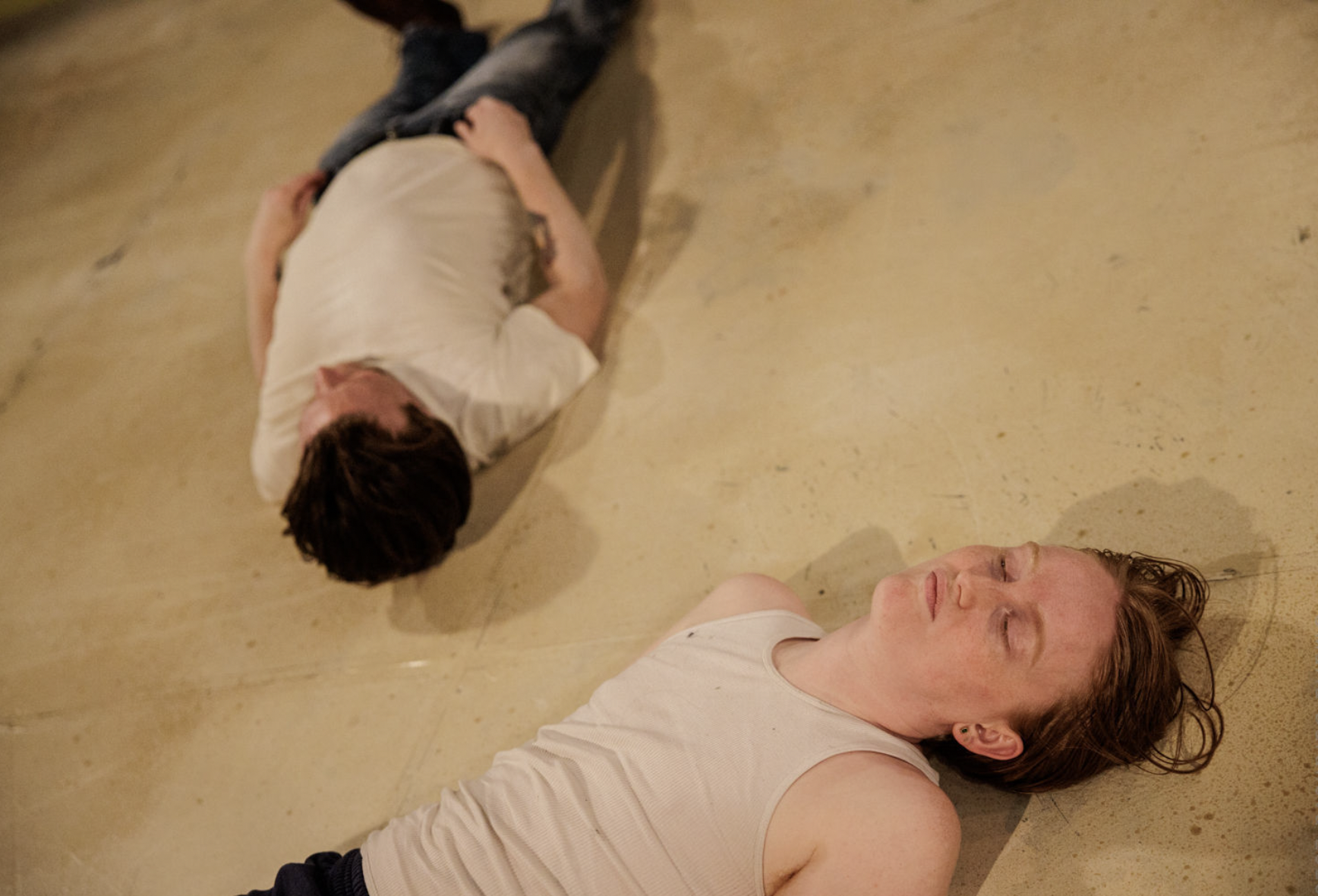 Two people in white shirts lie on a tan ground.