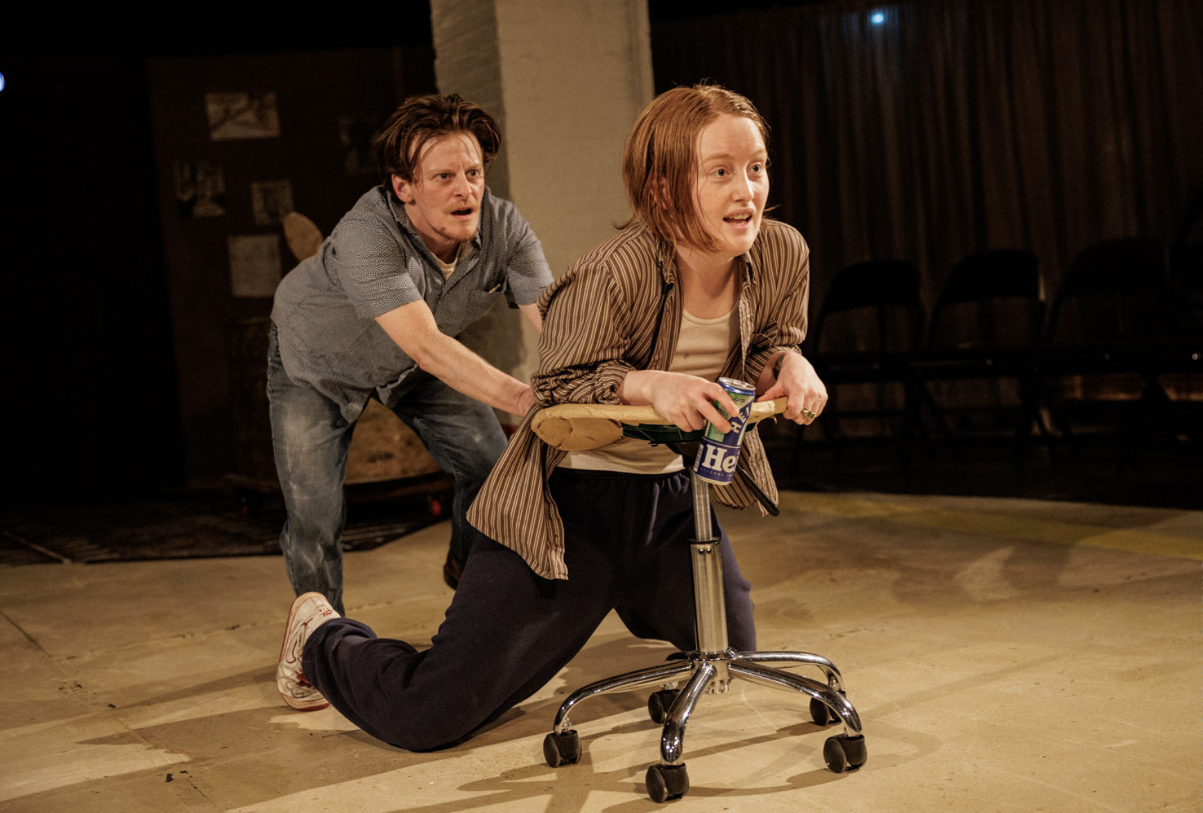 One person leans on a rolling stool as another pulls at their shirt