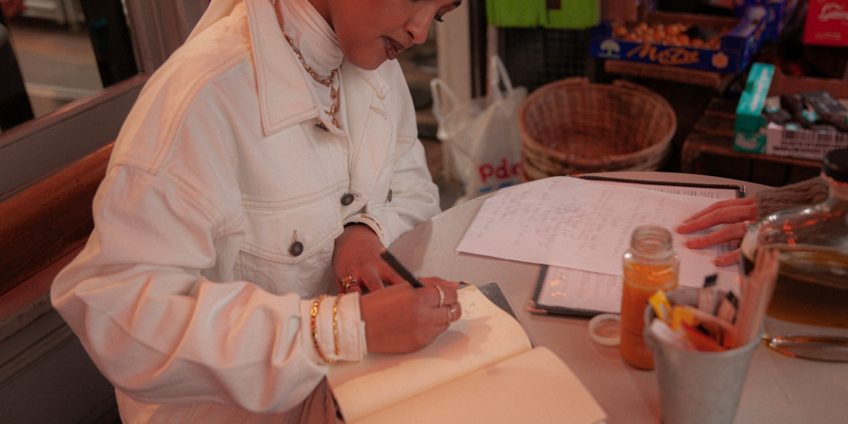 A woman writes in a notebook on a crowded cafe table