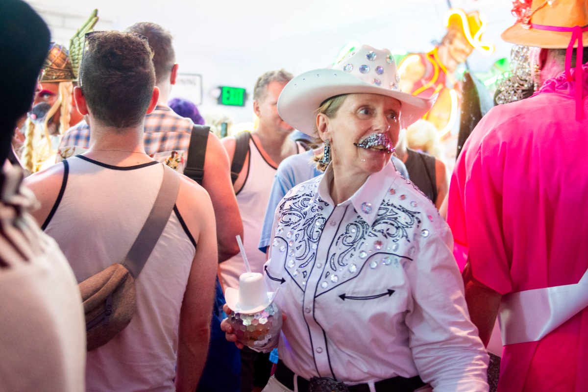 a queer person in a cowboy getup with gliterry moustach