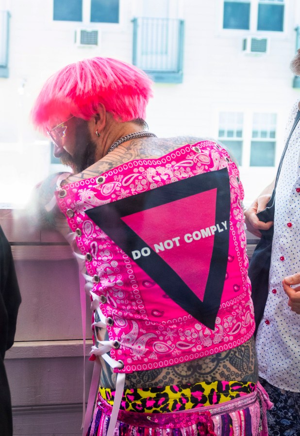 someone in a pink wig wears a vest that says DO NOT COMPLY