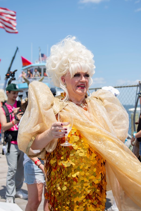 a drag queen in a gold dress holds a glass of water