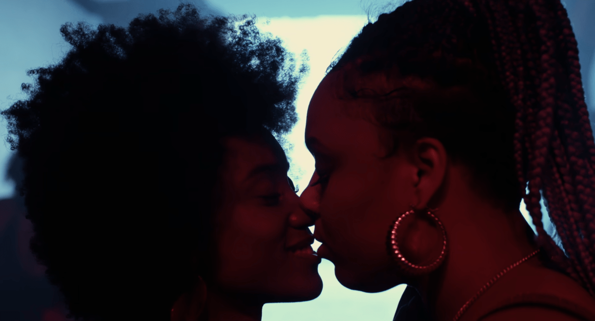 The best lesbian club scenes: Two women kiss in a club with a glowing blue light behind them