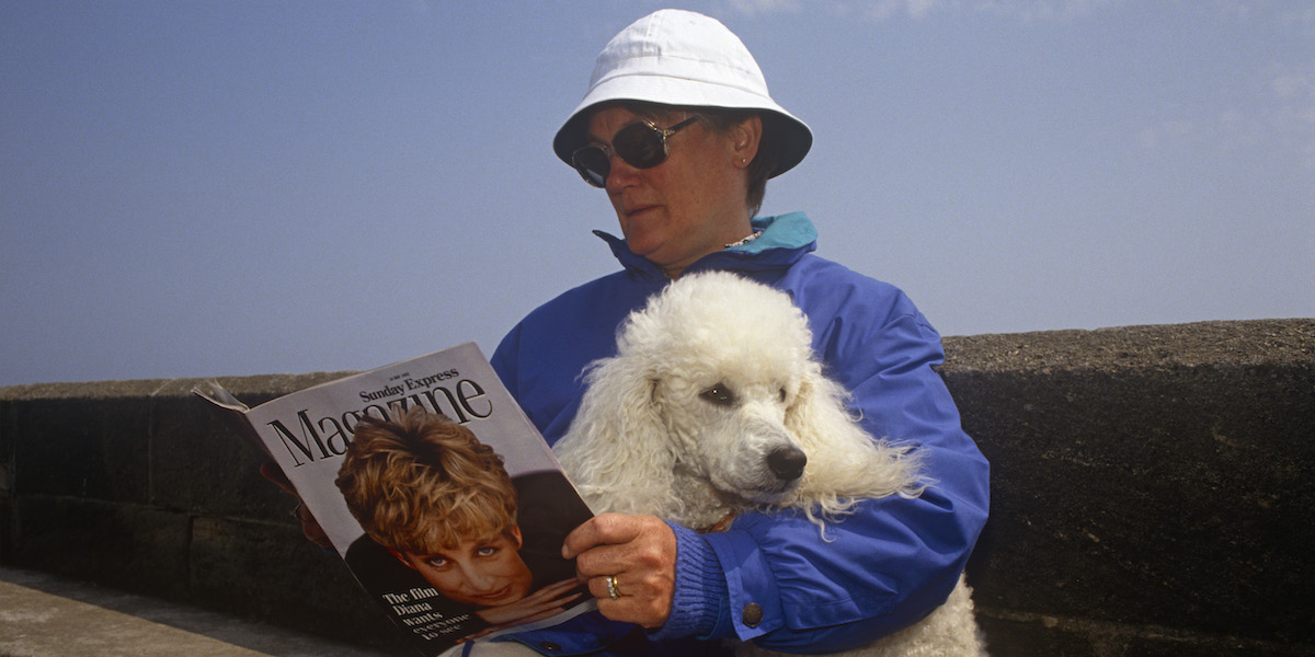 A 1990s lady sits with her pet poodle on a sea wall reading the Sunday Express magazine that features Princess of Wales on the cover, on 19th July 1993, at Scarborough, North Yorkshire, England. (Photo by Richard Baker / In Pictures via Getty Images)
