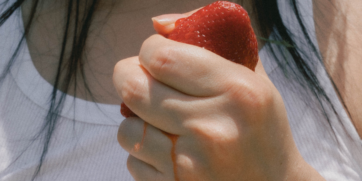 a hand squeezing a strawberry